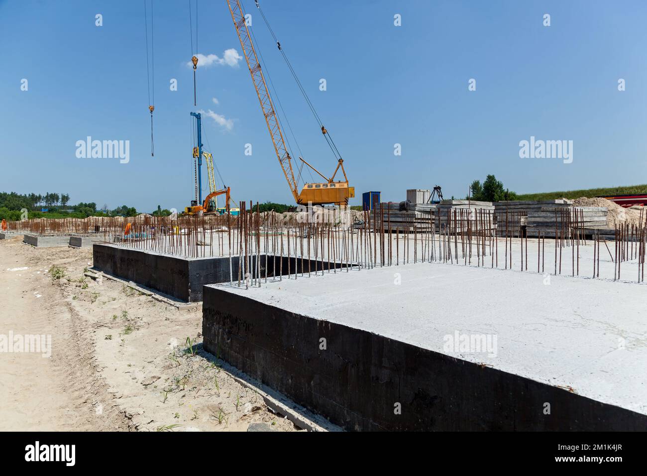 Cantiere con attrezzature, rimessa e fondazione di un edificio residenziale. Strutture in barre di cemento armato in acciaio per calcestruzzo Foto Stock