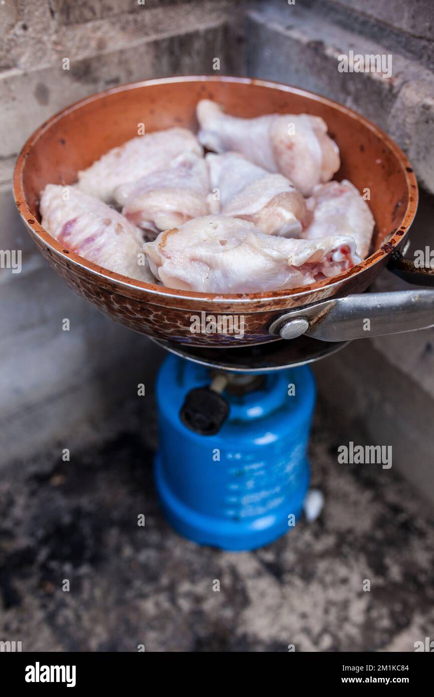 Pasto spagnolo all'aperto. Ali di pollo fresche che friggono su una padella in una stufa a gas da campeggio Foto Stock