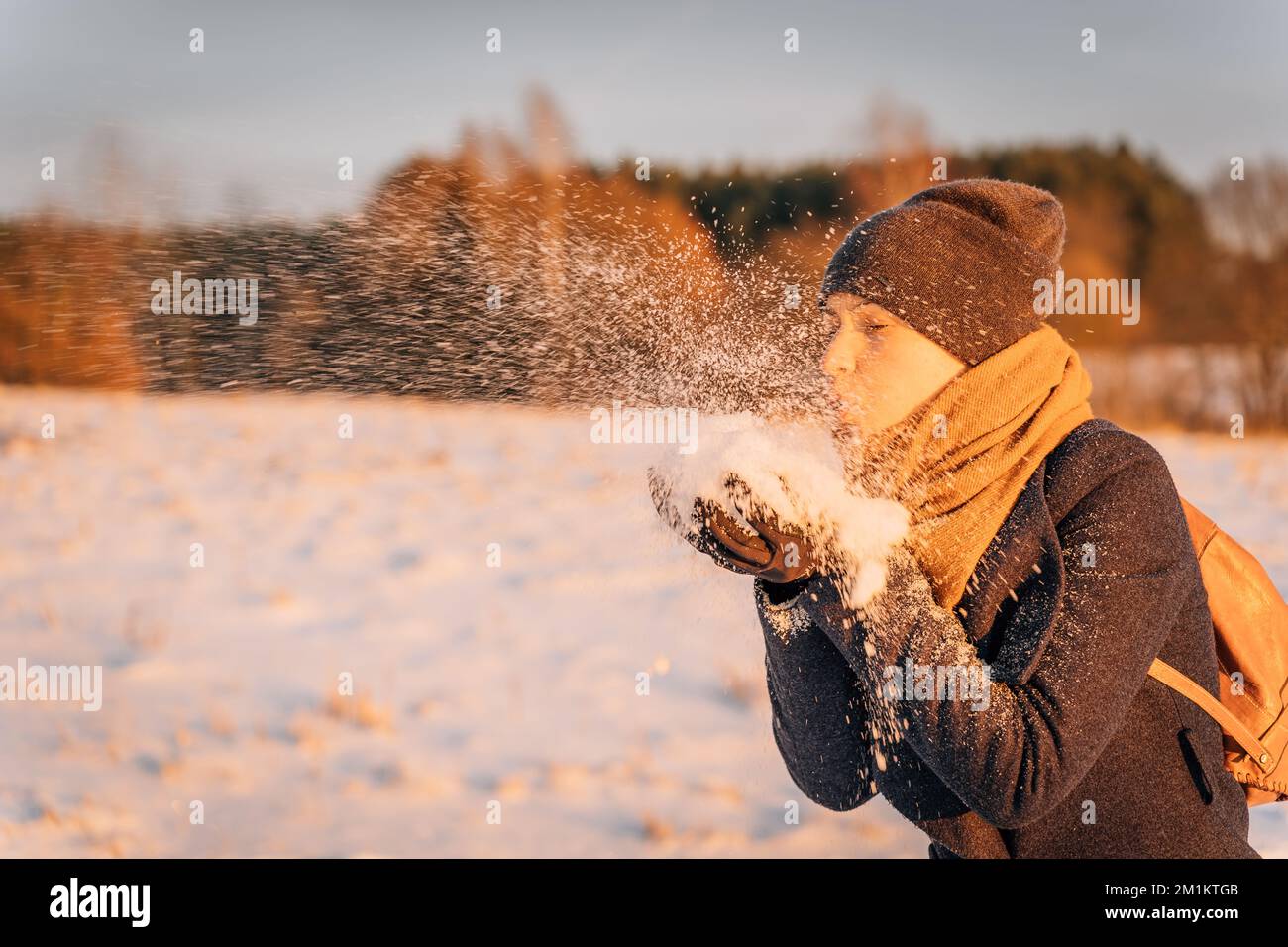 Una donna soffia una manciata di neve dalle sue mani al tramonto di sera Foto Stock