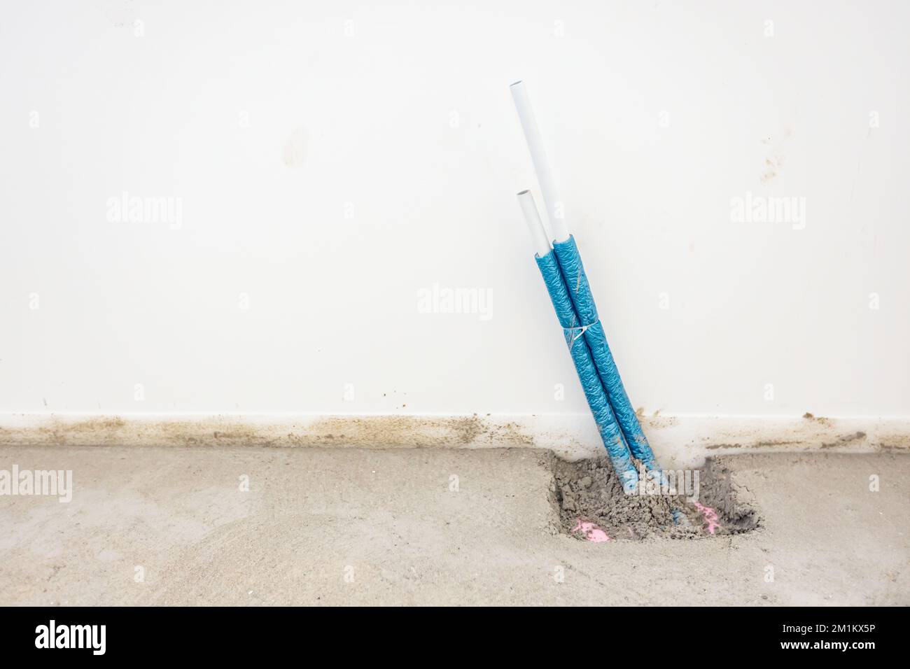 Un fascio di tubi flessibili in plastica blu isolati fuoriesce da un pavimento in cemento montato per il riscaldamento centralizzato in un edificio residenziale in costruzione. Foto Stock