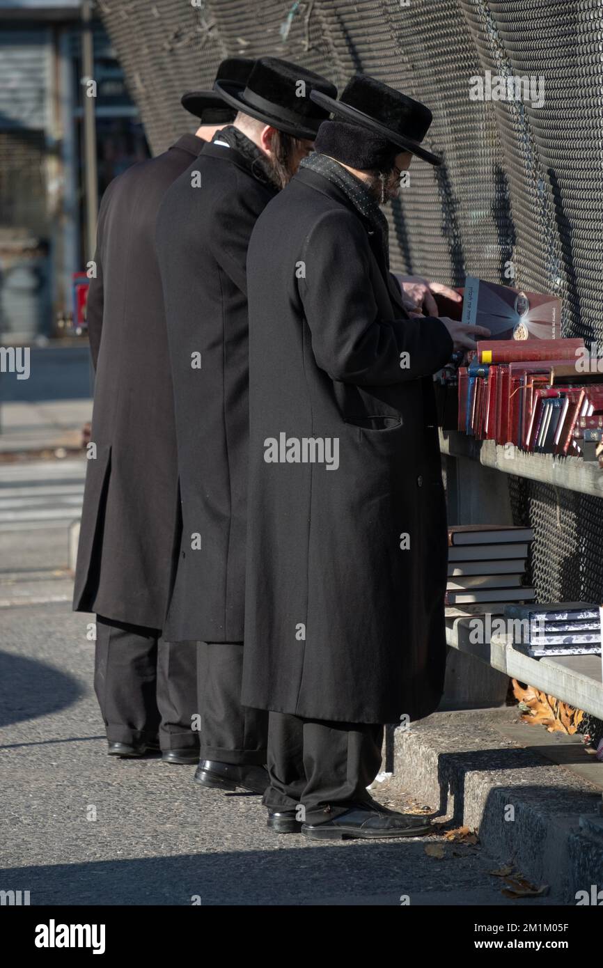 Tre uomini ebrei ortodossi vestiti allo stesso modo sfogliano libri religiosi in una vendita all'aperto a Brooklyn, New York City. Foto Stock