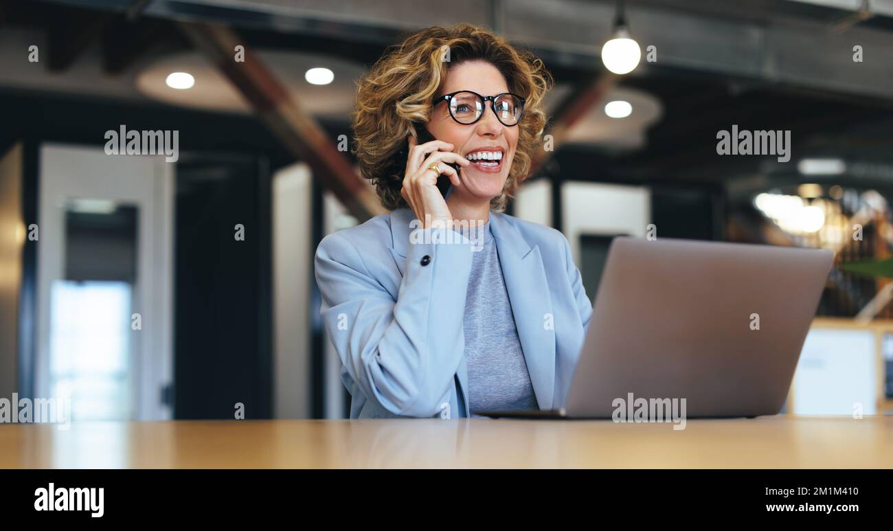 donna d'affari che parla al telefono in un ufficio di coworking. Una donna felice che chiama i suoi colleghi su un telefono cellulare. Aziende professionali Foto Stock