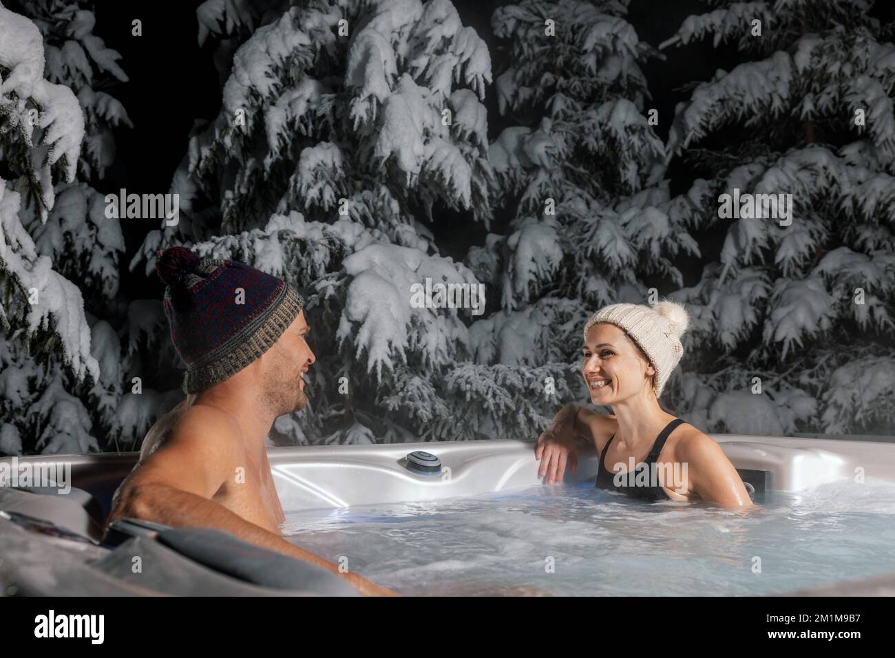 una coppia felice si rilassa nella vasca idromassaggio all'aperto in inverno con alberi innevati sullo sfondo. centro benessere Foto Stock