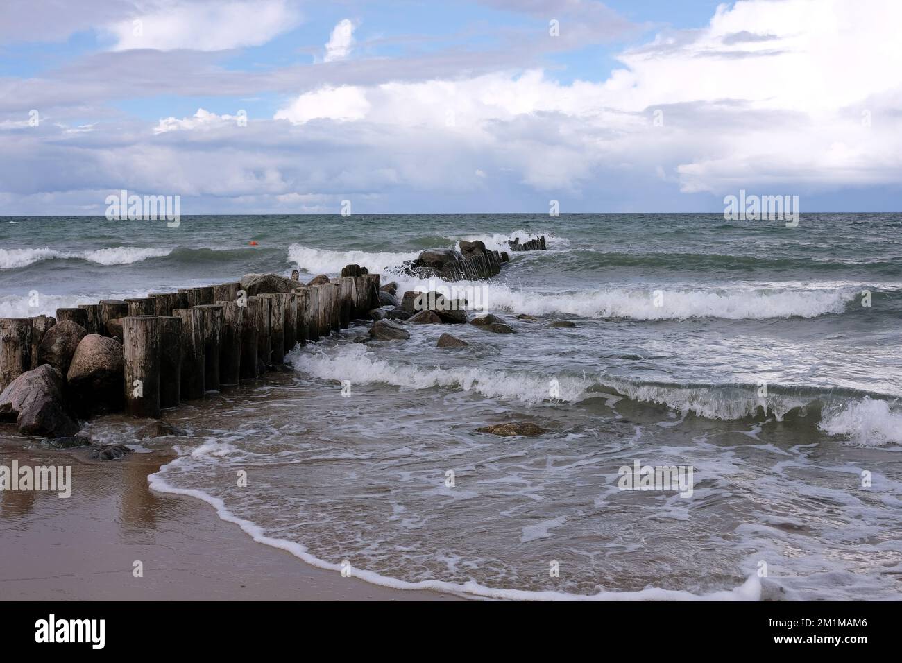 Paesaggio di mare con tronchi di legno come Wavebreaker andando lontano nel mare tempestoso sotto le nubi grigie e pesanti di pioggia in giorno ventoso Foto Stock