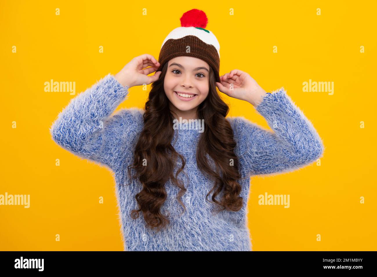 Bel ritratto invernale per bambini. Ragazza adolescente in posa con maglione invernale e cappello a maglia su sfondo giallo. Felice adolescente, positivo e sorridente Foto Stock