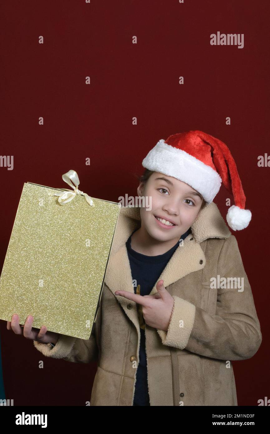 Banner verticale di Natale con una ragazza adolescente in un cappello di Babbo Natale e una borsa regalo dal negozio. sfondo rosso scuro. posiziona per testo Foto Stock