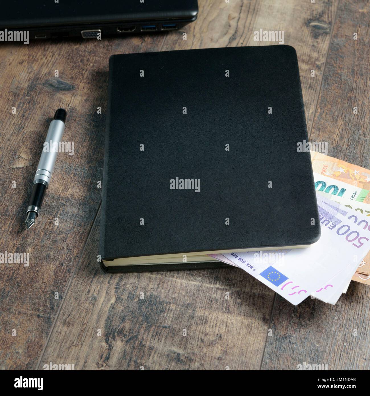 Frammento di libro contabile di un dispositivo di conto con banconote in euro e una penna stilografica sullo sfondo di un tavolo di legno. Foto Stock