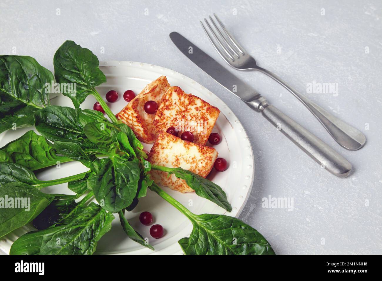 Mozzarella alloumi alla griglia con spinaci verdi e mirtilli rossi su un tavolo grigio in cemento Foto Stock