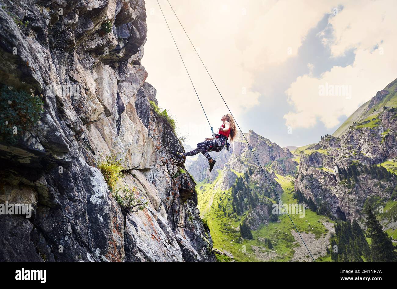 Misura forte donna arrampicatore che vola in aria vicino ad alta roccia verticale con corda alle montagne in Kazakistan Foto Stock