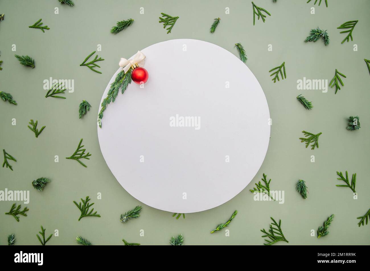 Composizione di Natale. Rami di abete, thuja, ginepro, abete rosso cipresso su fondo verde. Bianco round ad spazio podio mock up con palla rossa. Chris Foto Stock
