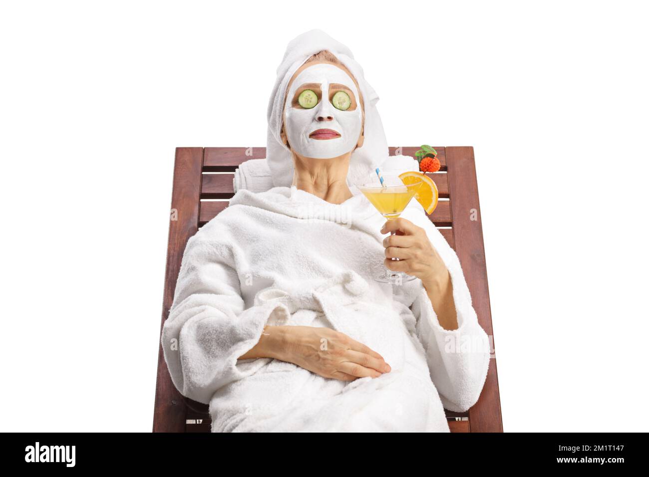 Donna in accappatoio con maschera facciale e cetriolo sugli occhi rilassante con un cocktail isolato su sfondo bianco Foto Stock