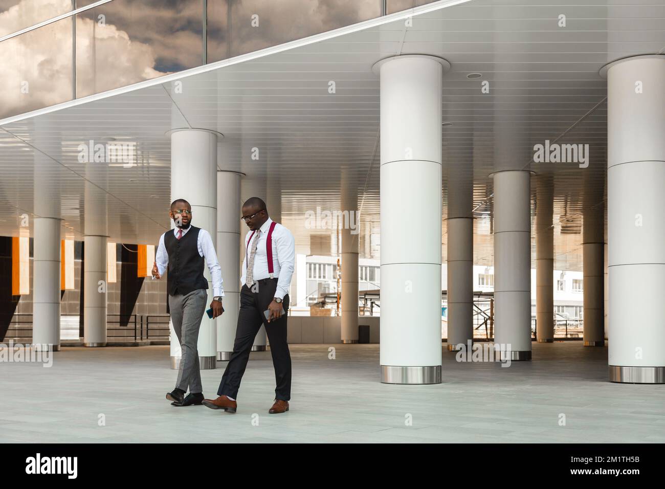 Ritratto di due uomini d'affari dalla pelle scura che camminano e parlano davanti ad un edificio moderno esterno. Meeting all'aperto Foto Stock