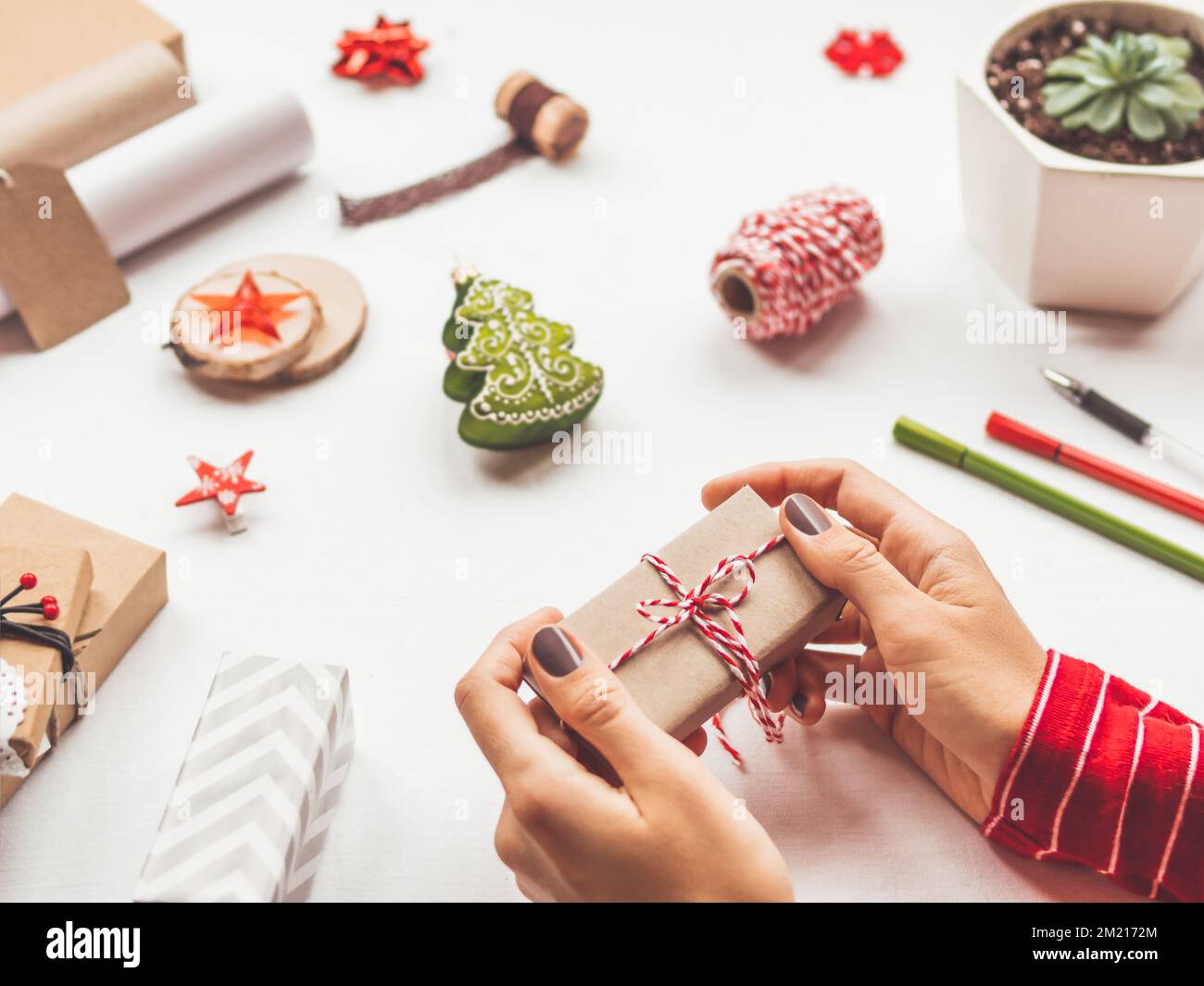 Tavolo bianco con decorazioni natalizie. Donna avvolge il regalo di Capodanno su carta artigianale. Spirito di vacanza invernale. Foto Stock