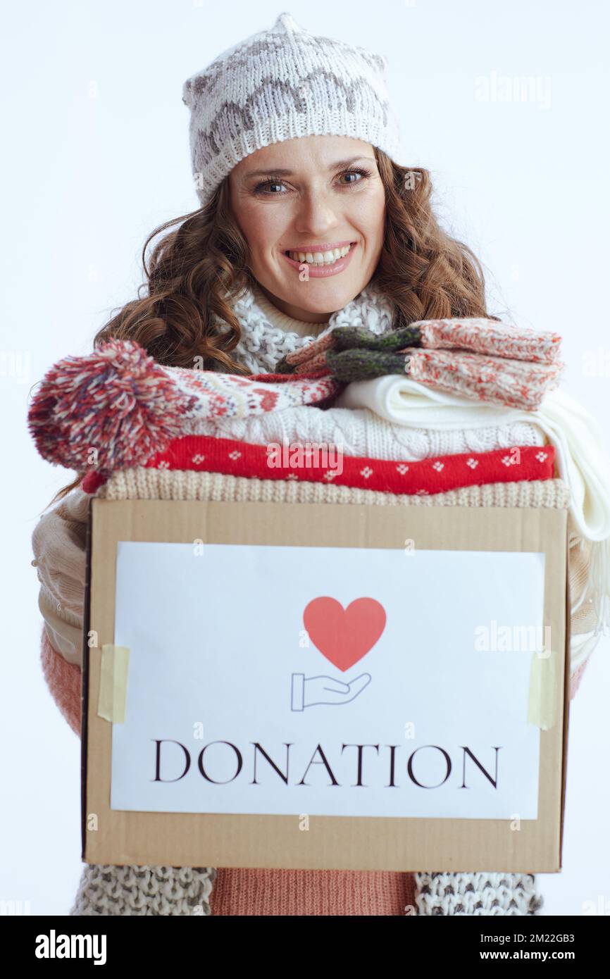 Ciao inverno. donna moderna felice di 40 anni in maglione, guanti, cappello e sciarpa su sfondo bianco con scatola di donazione. Foto Stock