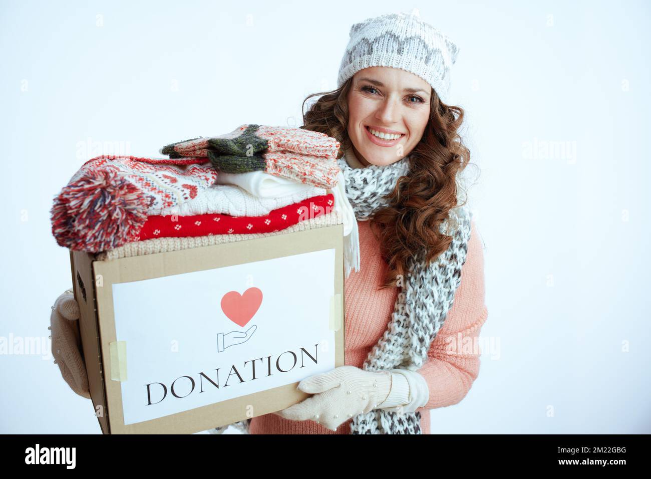 Ciao inverno. donna sorridente alla moda in maglione, guanti, cappello e sciarpa isolato su sfondo bianco con scatola di donazione. Foto Stock