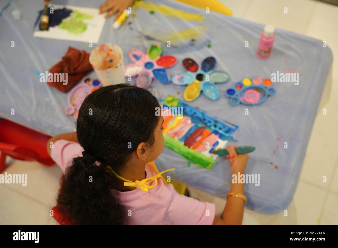 Piccola ragazza dipingere con pitture colorate utilizzando pennelli e tavolozze di colore in classe. Concetto di creatività e sviluppo per i bambini Foto Stock