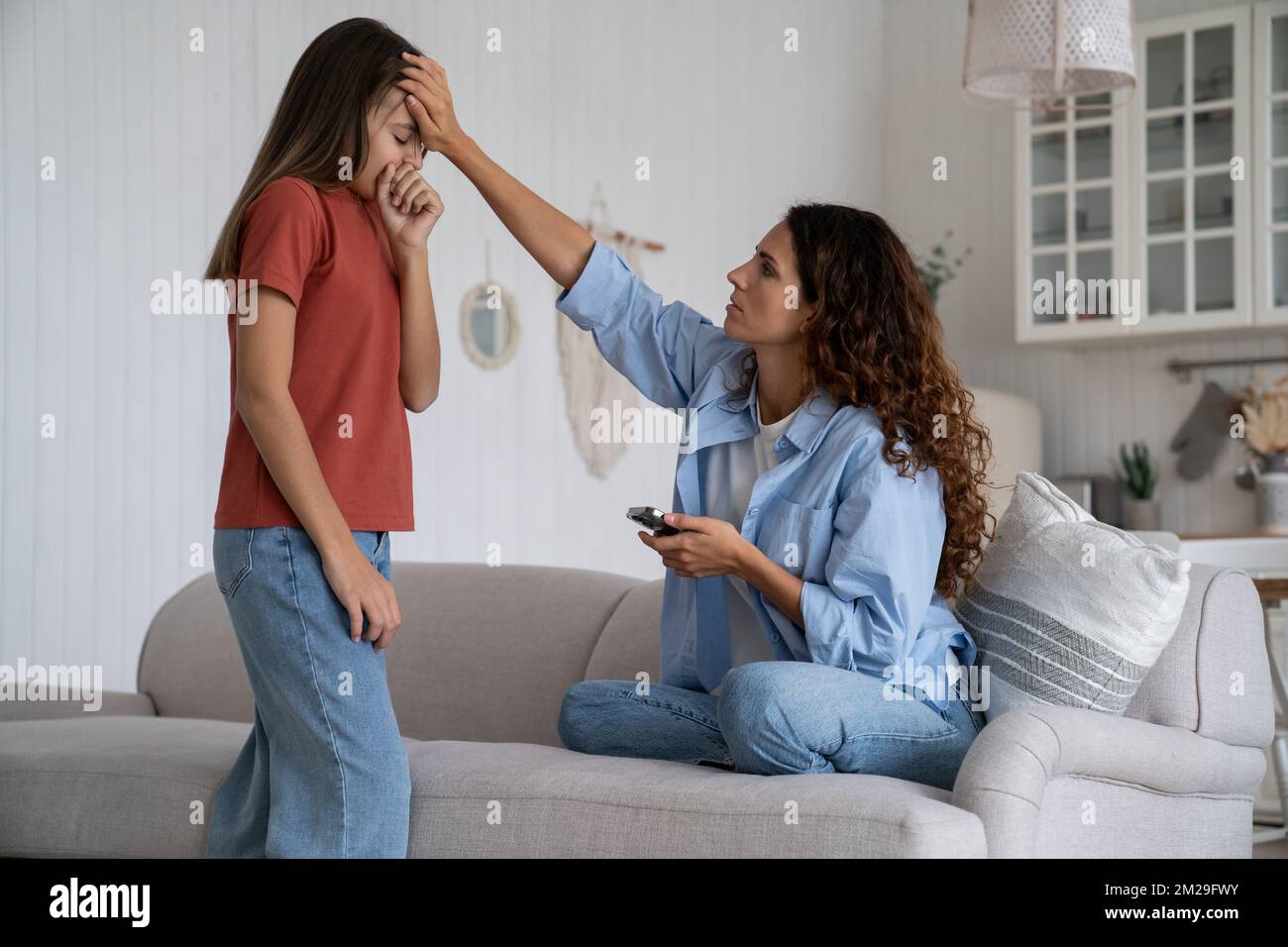 Madre preoccupata che tiene il telefono che tocca la fronte della figlia malata, che chiama il medico pediatra Foto Stock