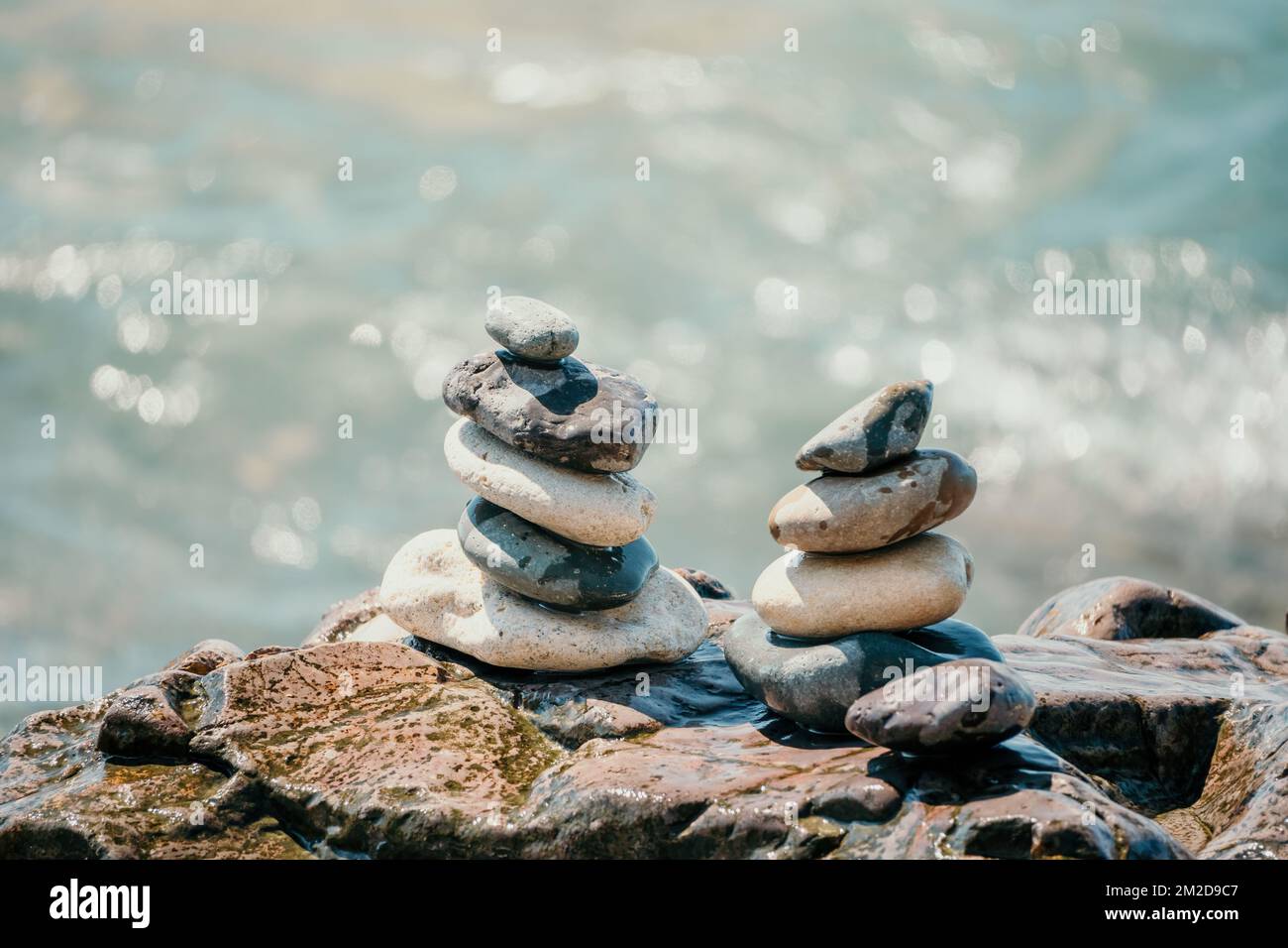 Piramide di roccia bilanciata sulla spiaggia di ciottoli, giorno di sole e cielo limpido al tramonto. Bokeh Golden Sea sullo sfondo. Fuoco selettivo, pietre zen sulla spiaggia di mare Foto Stock