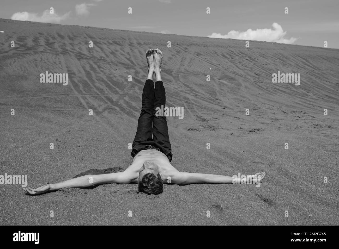 Lone uomo sdraiato sulla sabbia con le gambe in alto nel deserto Foto Stock