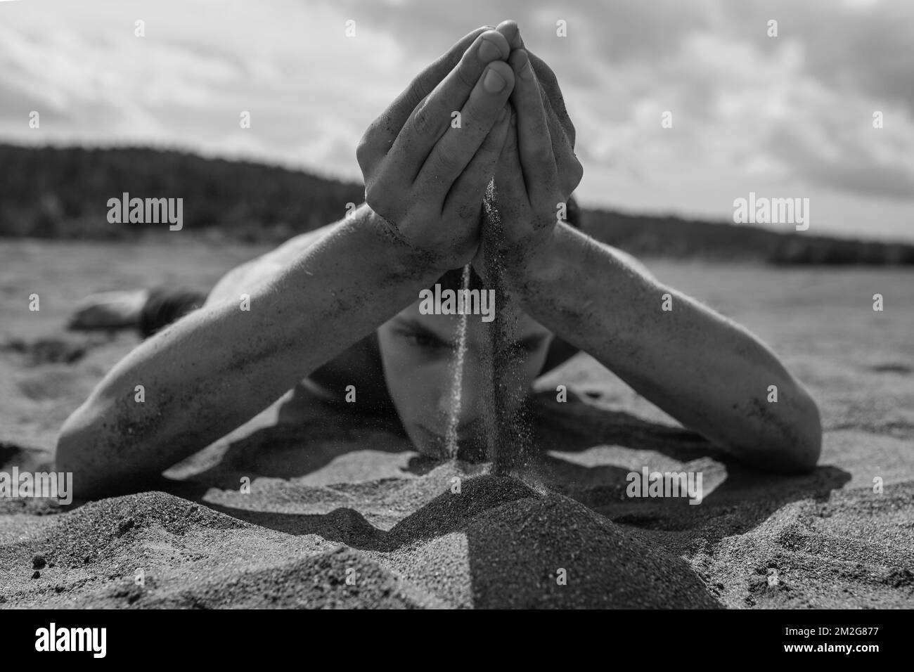 L'uomo giace sullo stomaco e versando sabbia attraverso le mani nel deserto Foto Stock