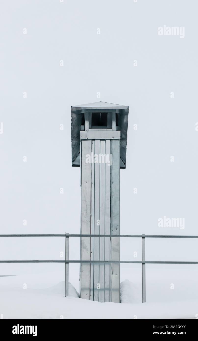 Fumo, tubo di scarico rettangolare sul tetto di una casa moderna. Il tetto dell'edificio è coperto di neve bianca contro il cielo grigio. Nuvoloso, freddo giorno d'inverno, luce soffusa. Foto Stock