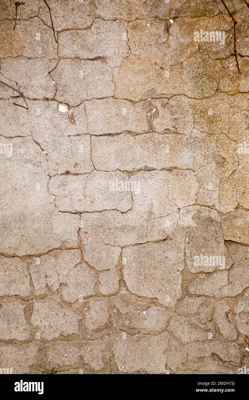 Foto di una parete con intonaco fessurato - sfondo del materiale. Un'immagine vintage di un vecchio muro di scabchiera con crepe irregolari e non simmetriche - un'immagine per uno sfondo artistico. Luce calda e soffusa. Foto Stock