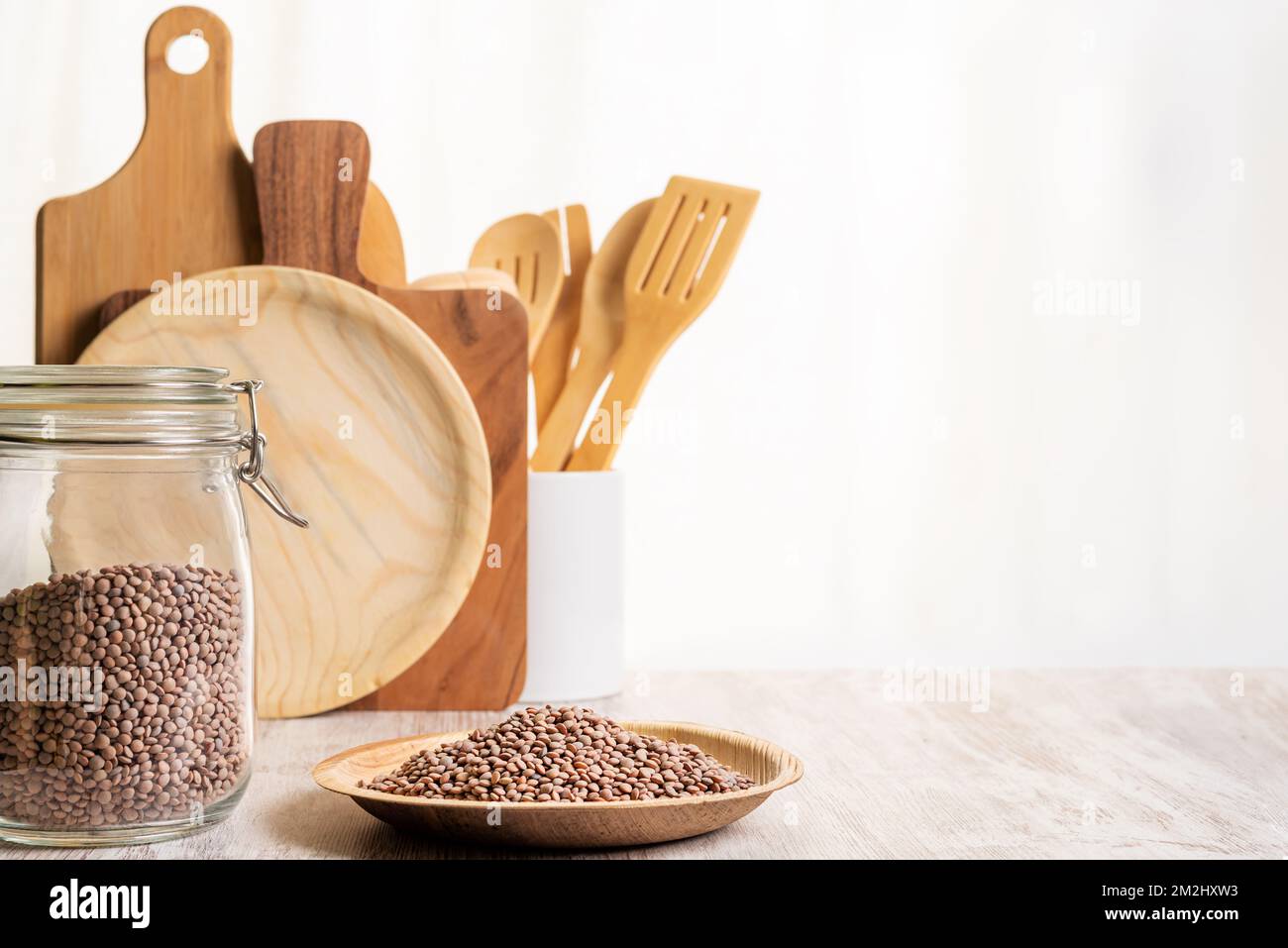 Vaso da cucina con lenticchie accanto a un piatto con lenticchie non cotte, dietro taglieri e utensili da cucina. Foto Stock