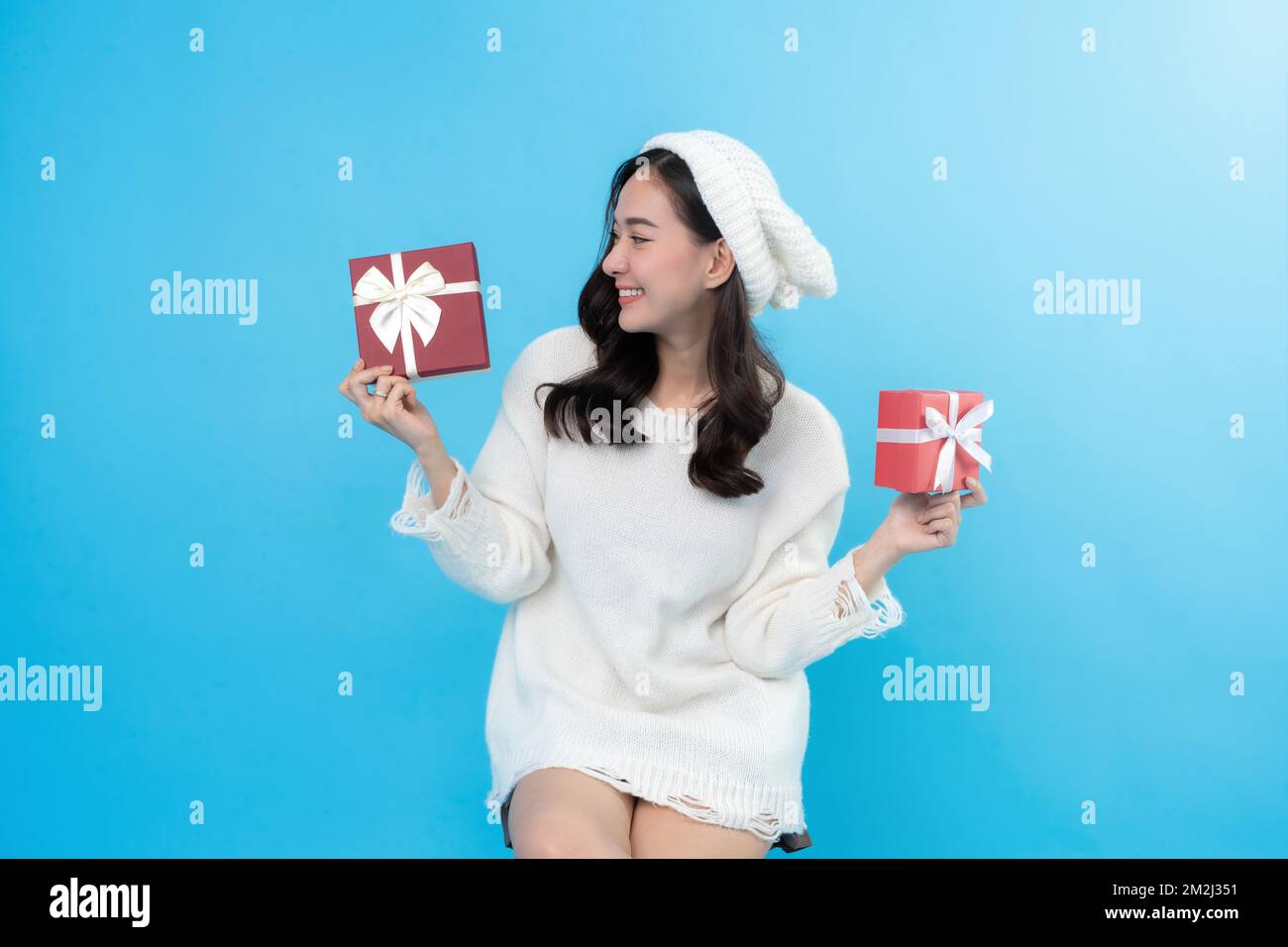 Donna felice su sfondo blu a natale indossando un cappotto bianco e cappello per celebrare il festival di Capodanno pronti a dare meravigliosi regali per tutti Foto Stock