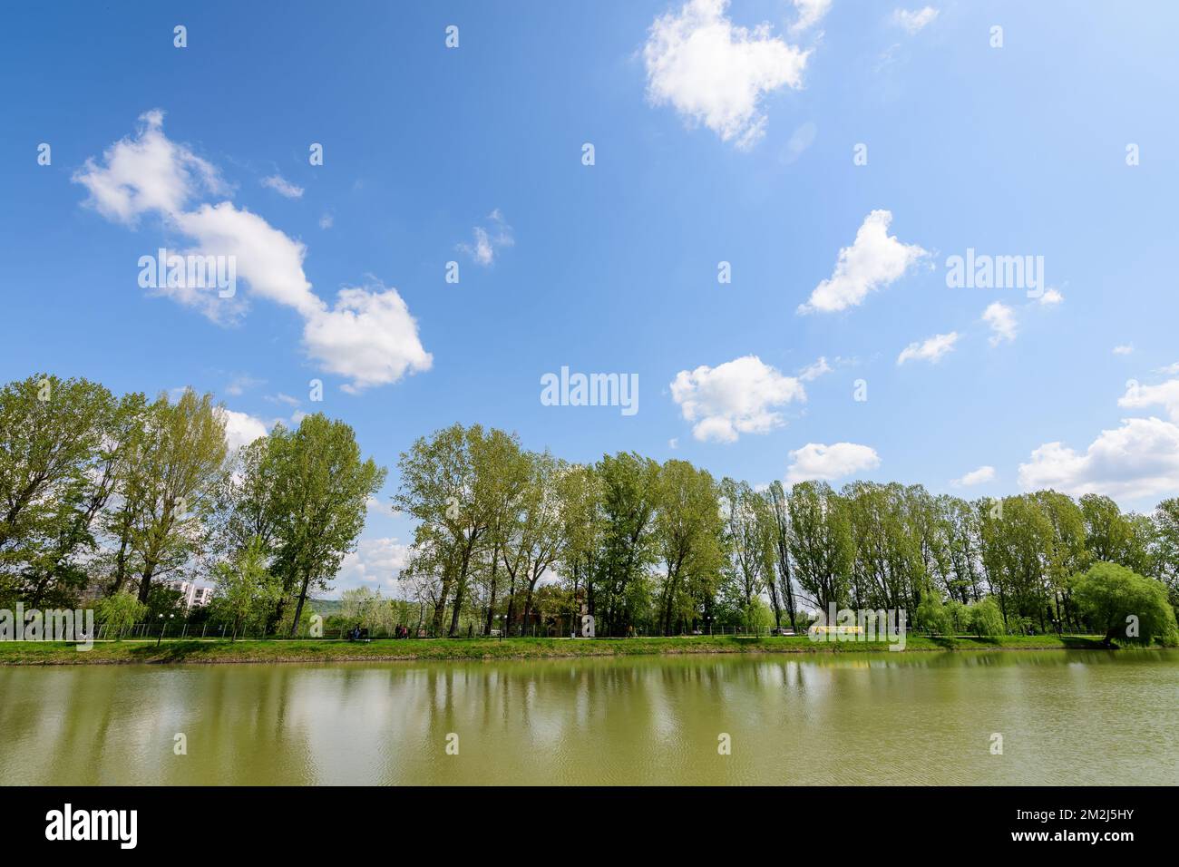 Piccolo lago con un mulino a legna e un'isola dal Parco Chindiei (Parcul Chindiei) a Targoviste, Romania, in una soleggiata giornata primaverile con nuvole bianche e blu Foto Stock