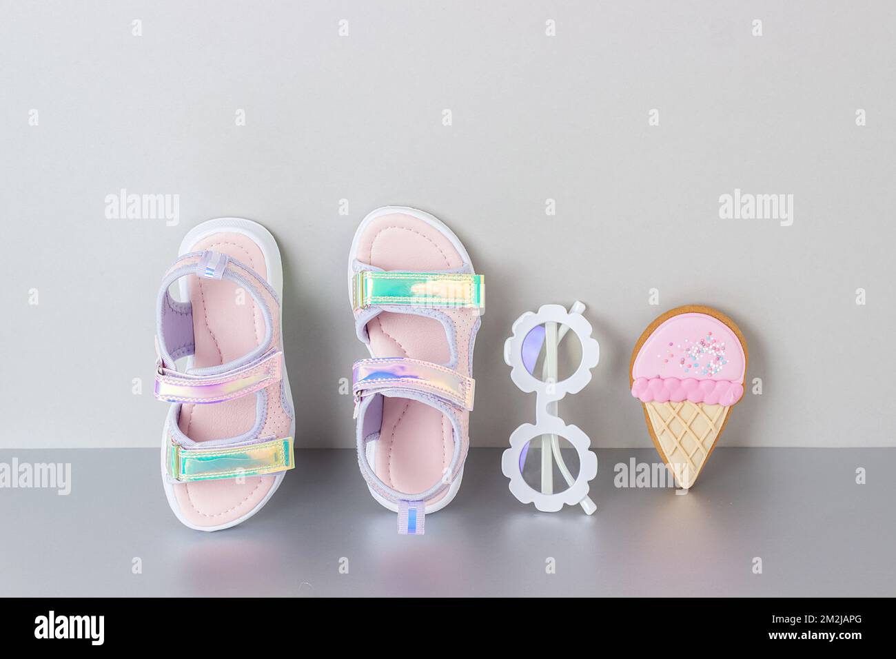 Eleganti sandali olografici per bambini su sfondo grigio. Scarpe estive alla moda lucenti. Foto Stock