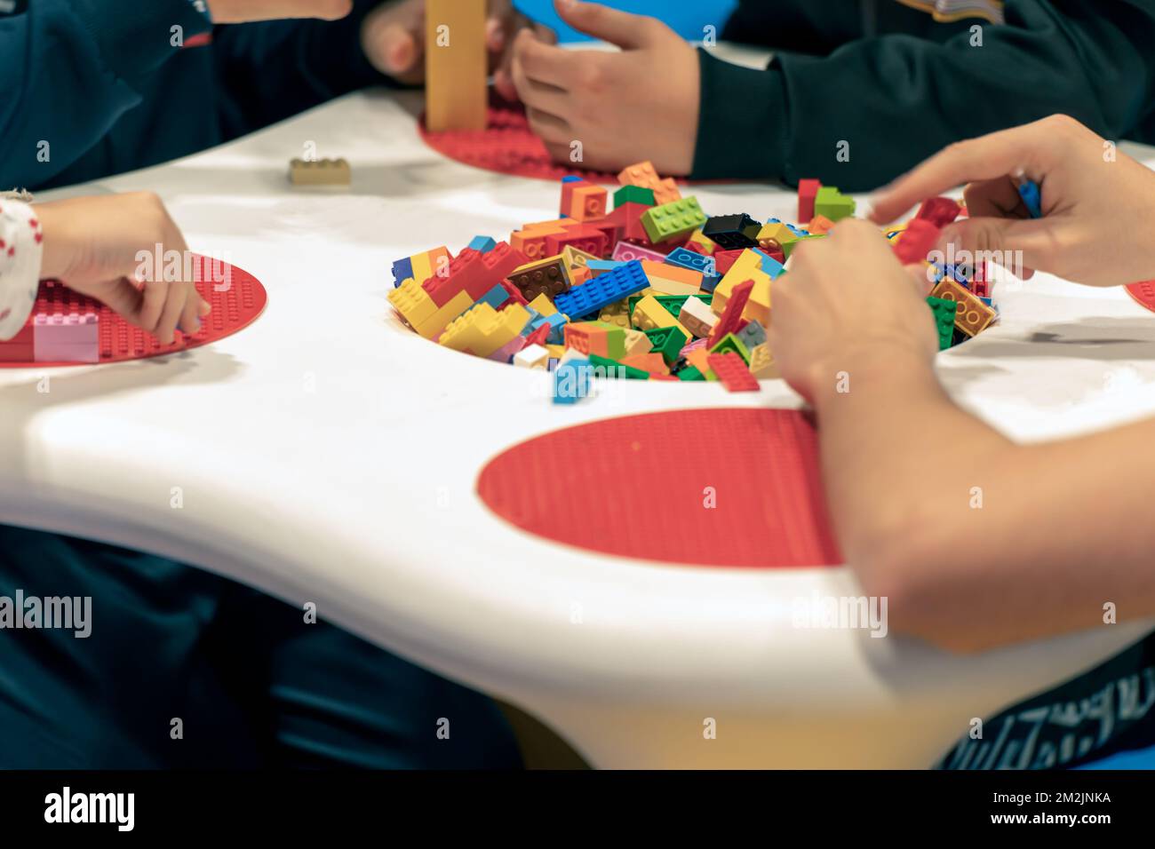 Gruppo di bambini raccolti seduti al tavolo e giocando con mattoni colorati il giorno del fine settimana in sala giochi Foto Stock