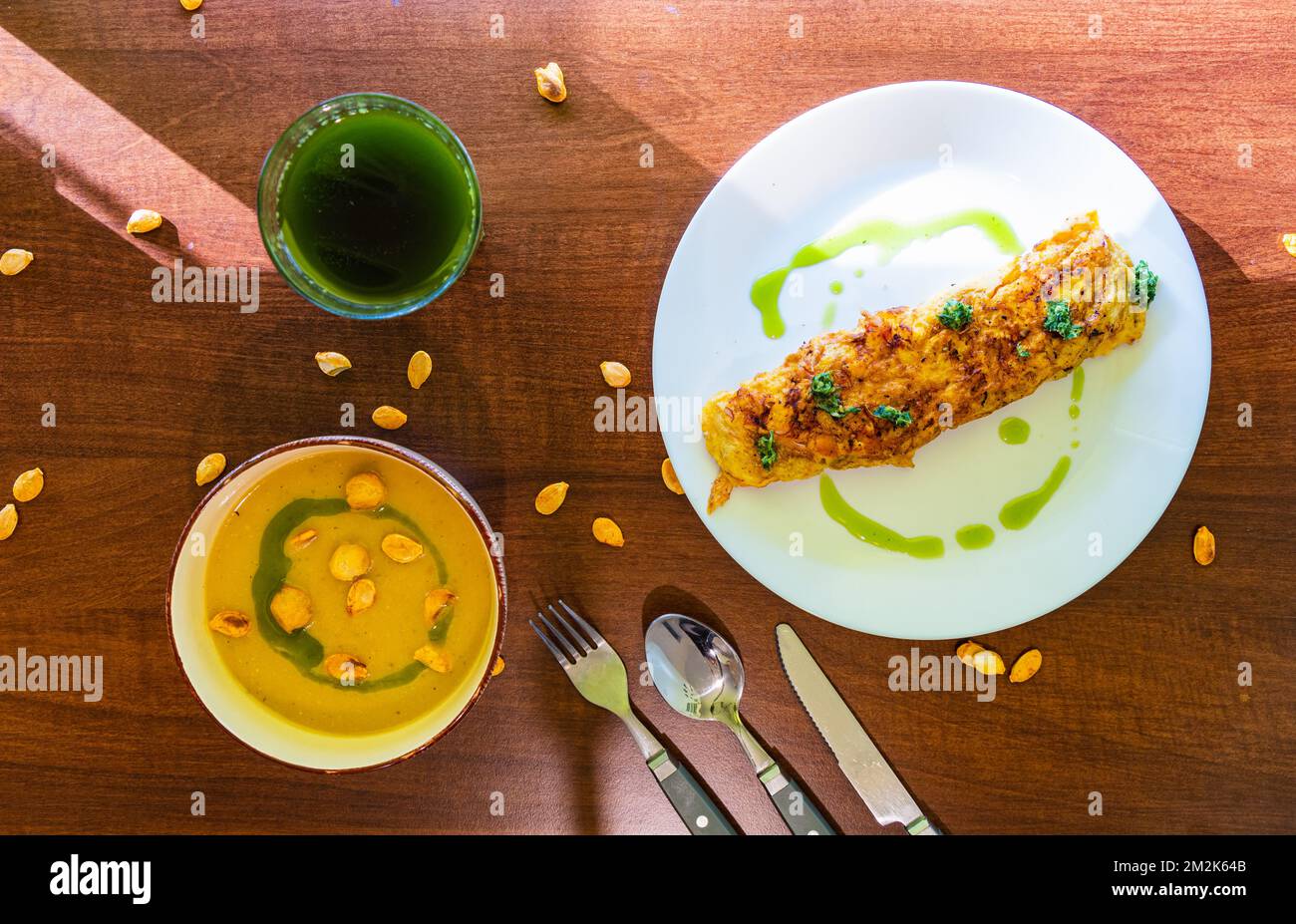 Vista dall'alto verso il basso sul tavolo da cucina con pochi piatti come omelette all'uovo con prezzemolo e zuppa di crema di zucca e bicchiere di frullato verde Foto Stock