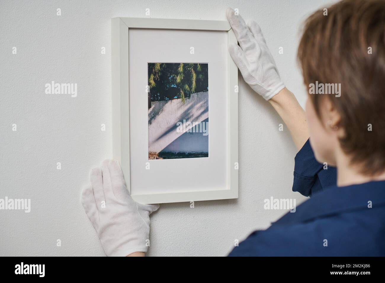 Vista posteriore della giovane donna che decora parete bianca con foto incorniciata Foto Stock