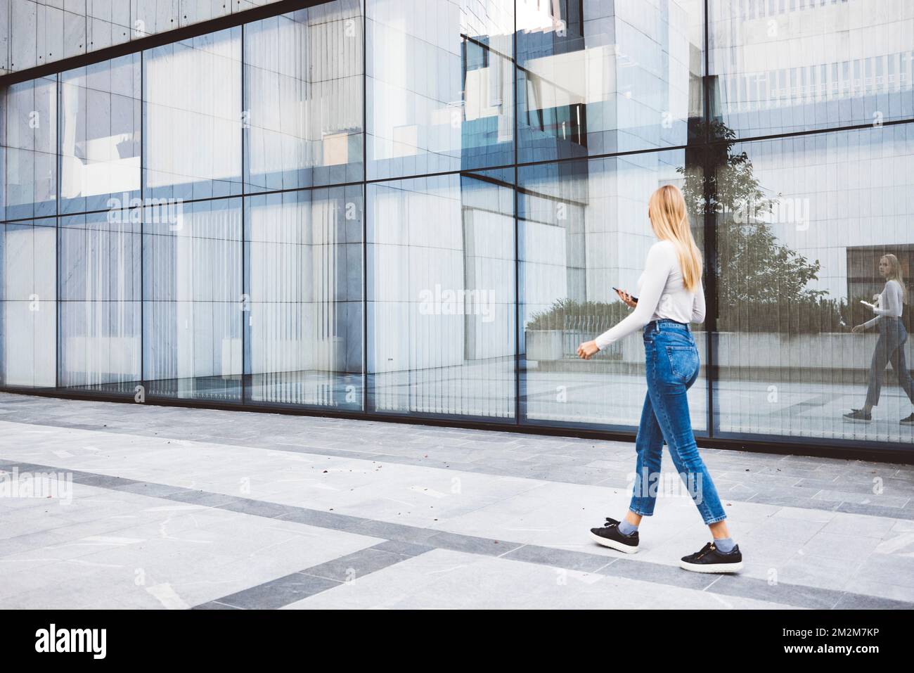 Donna che cammina accanto a un edificio di vetro per uffici durante una pausa Foto Stock
