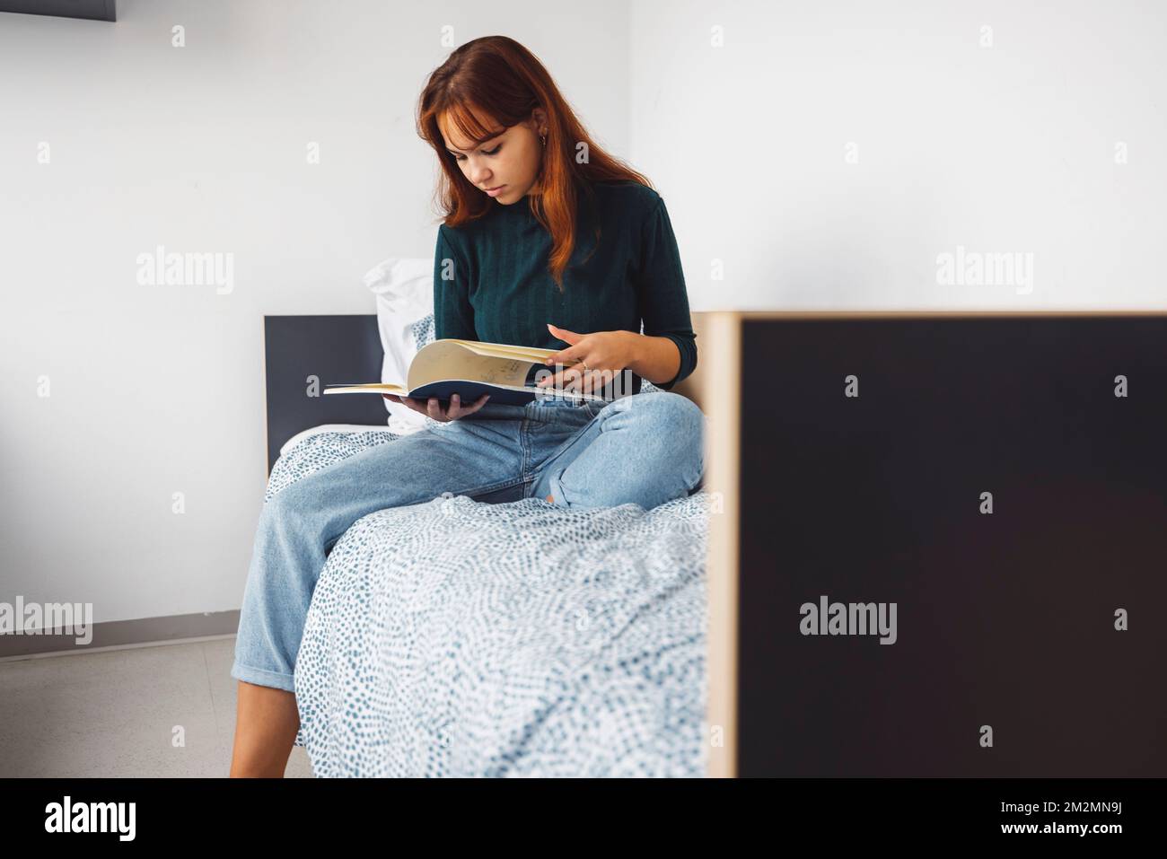 Giovane donna che studia musica leggendo un libro sul suo letto nella stanza del dormitorio Foto Stock