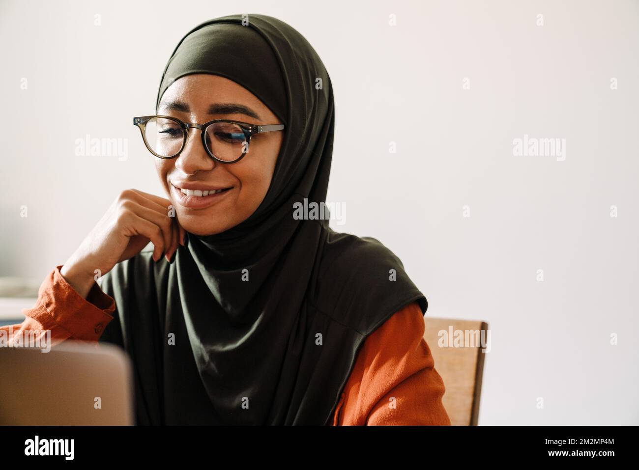 Giovane bella donna sorridente in hijab e gli occhiali che lavorano con il computer portatile primo piano Foto Stock