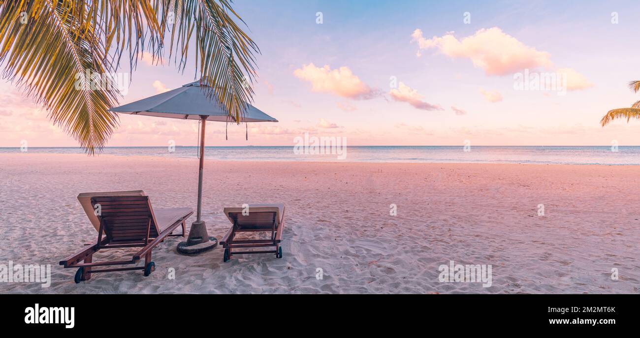 Panorama tropicale tramonto scenario, due lettini, lettini, ombrellone sotto la palma. Sabbia bianca, vista mare orizzonte colorato alba tramonto cielo Foto Stock