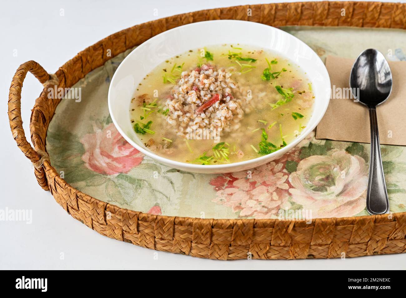 Brodo ricco di carne affumicata con pezzetto di carne con inguine su vassoio di fiori, cucchiaio su fondo bianco. Foto Stock