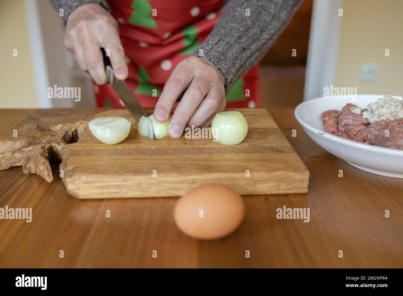 Le mani maschili a casa tagliano le cipolle su un asse di legno sul tavolo da cucina Foto Stock