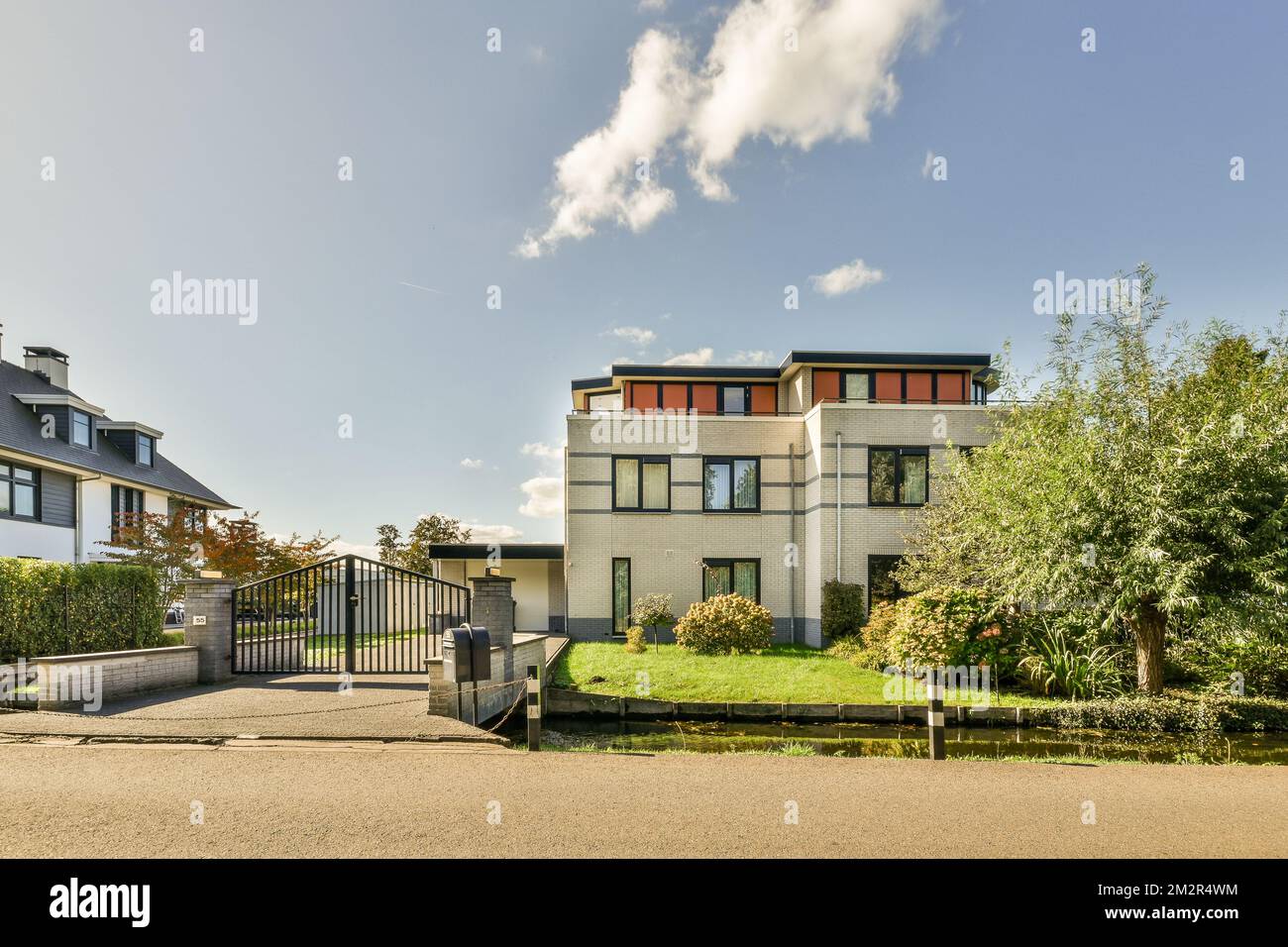 una casa nel mezzo di un quartiere urbano con alberi, arbusti e cespugli su entrambi i lati della strada Foto Stock