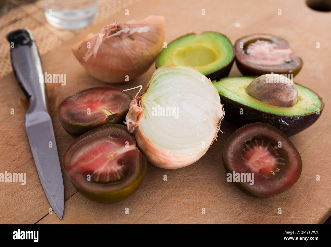 verdure pomodori neri, avocado e cipolle su tavola di legno Foto Stock