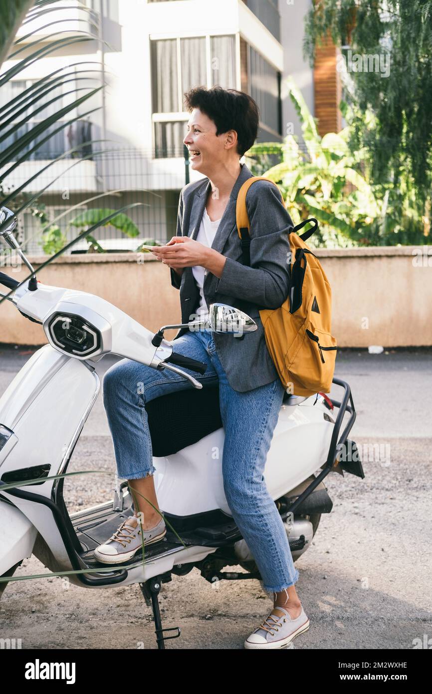 La donna di mezza età si prende sul suo scooter bianco. Foto Stock