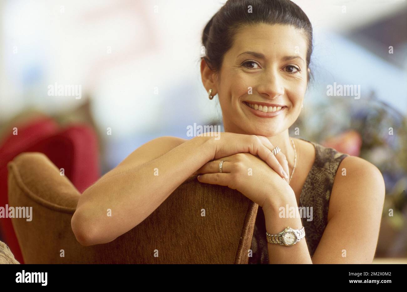 donna più giovane che pende dalla schiena di una sedia, sorridendo alla macchina fotografica Foto Stock