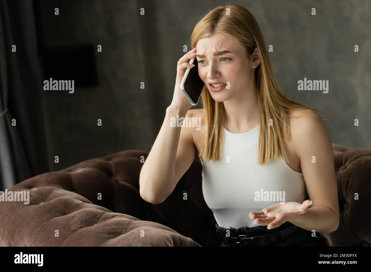 Donna preoccupata in cima a parlare sullo smartphone mentre si siede sulla poltrona a casa, immagine di scorta Foto Stock