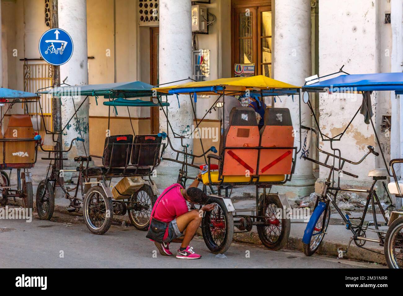 Un giovane cubano guarda il suo bicitaxi o pedicab. Il modo di trasporto urbano è una fonte importante di lavoro autonomo per i giovani in Th Foto Stock