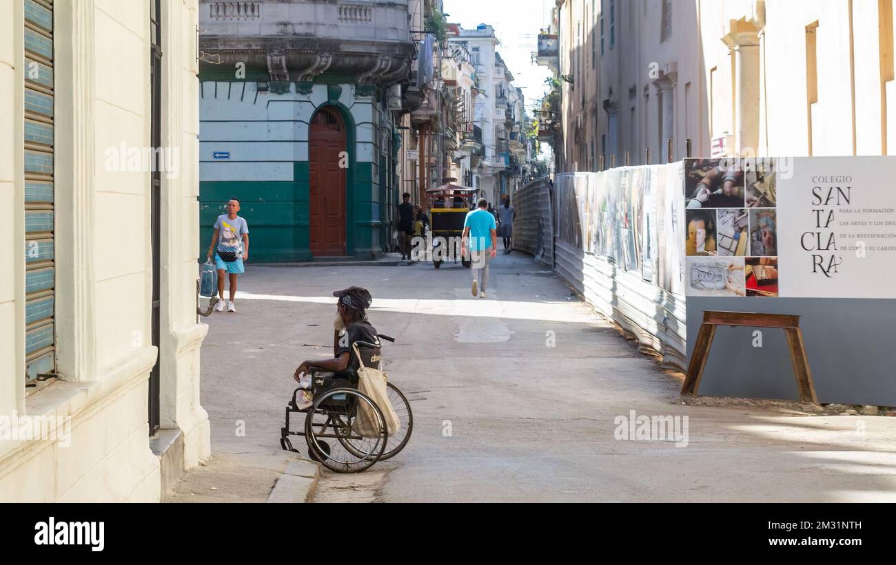 Un uomo afro-caraibico che vive con una disabilità si siede sulla sua sedia a rotelle in un angolo della città. Foto Stock