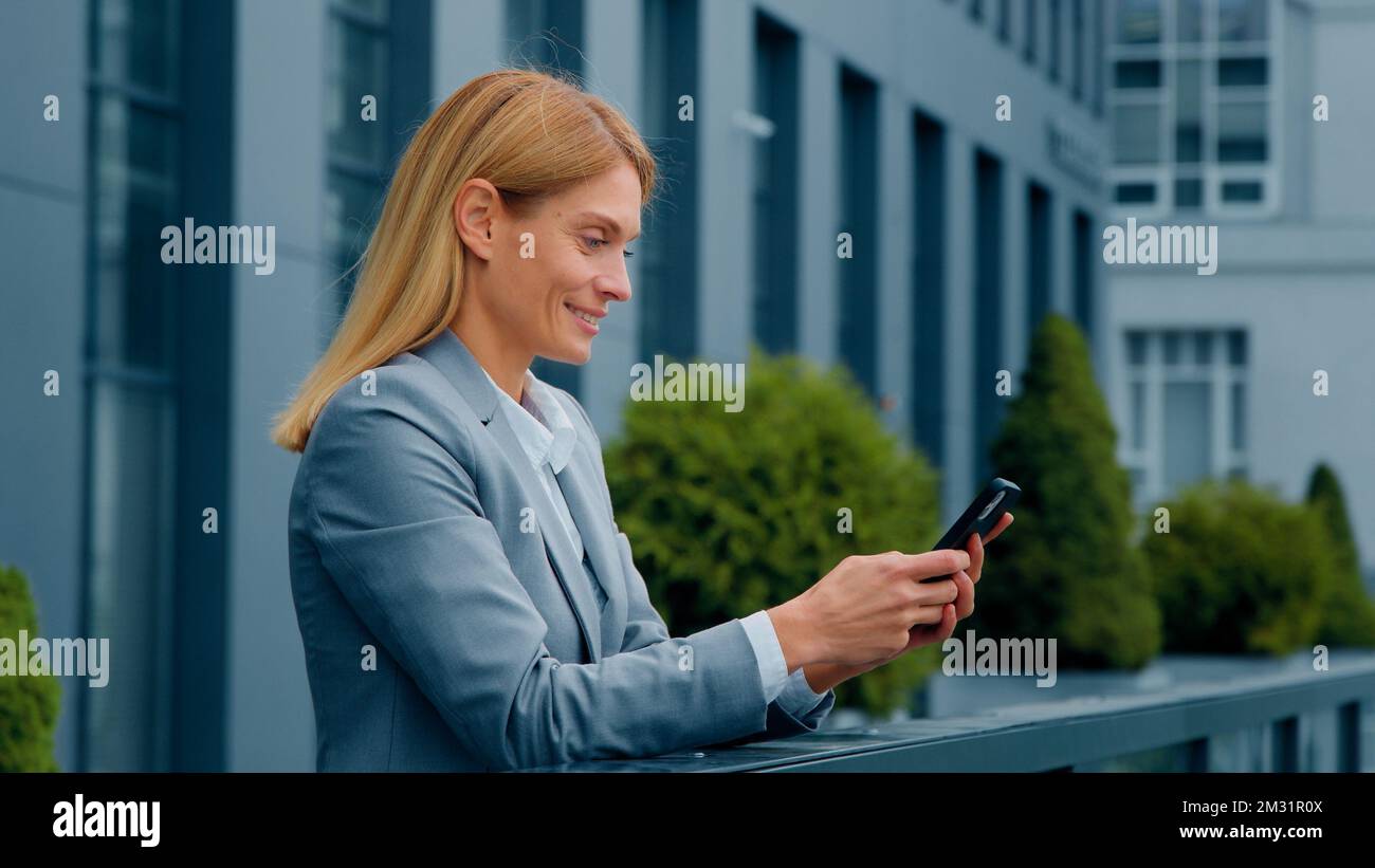 Sorridente donna attraente in piedi all'aperto che tiene il telefono che controlla il email che fa l'ordine nel deposito in linea donna felice d'affari che comunica nel sociale Foto Stock