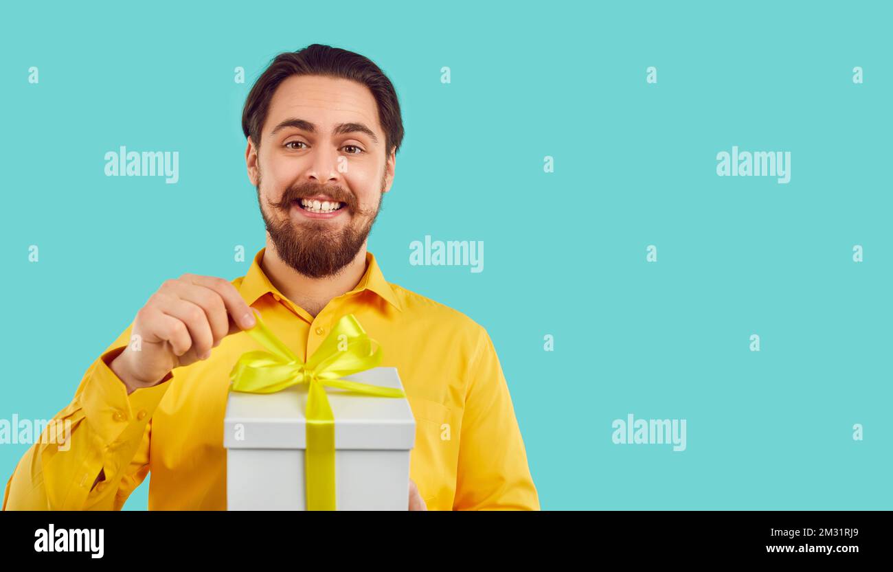 L'uomo eccitato con l'espressione felice unties l'arco sulla scatola del regalo isolata su fondo azzurro chiaro. Foto Stock