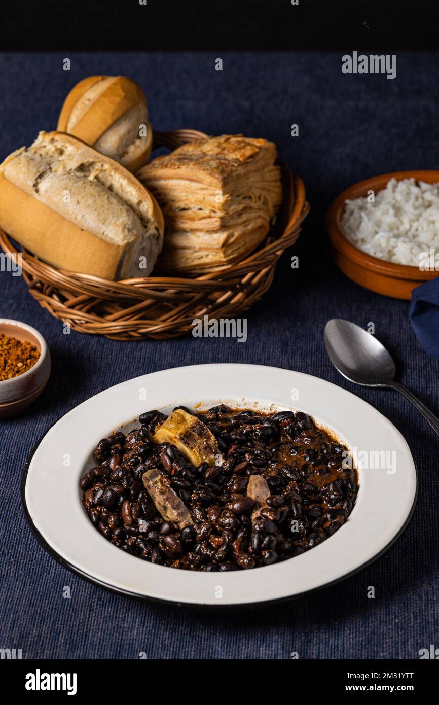 Fagioli e maiale, cibo tipico brasiliano, su tovaglia blu scuro. Foto Stock