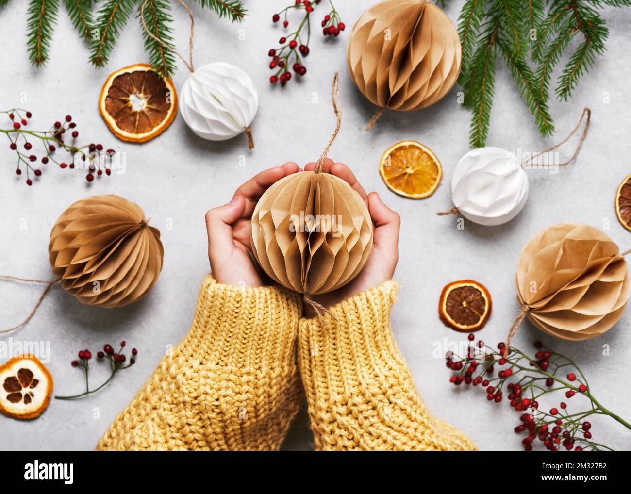 Palla di Natale in Honeycomb fatta a mano in bianco e marrone filtro caffè in mani ragazza. Scandinavian Nordic Craft Paper Concept. Vista dall'alto. Foto Stock